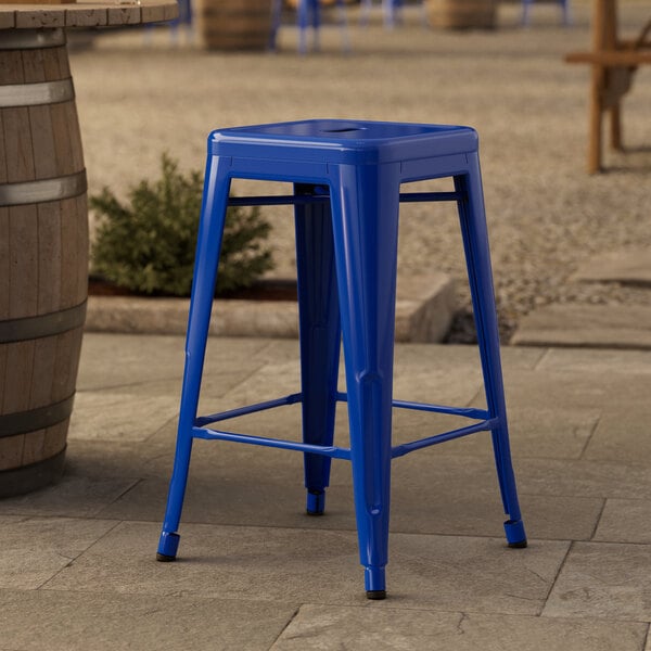 A blue Lancaster Table & Seating outdoor backless counter height stool on a stone surface.