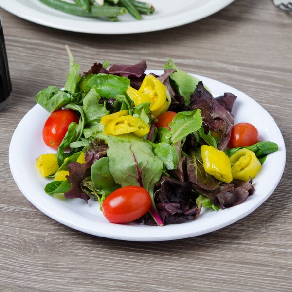 A Carlisle white melamine salad plate with salad on a table.