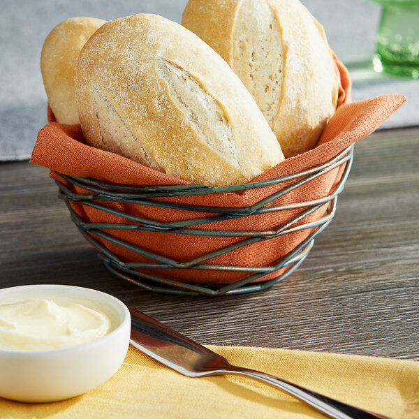 A Front of the House hand-painted fused iron round basket filled with bread and butter on a table.