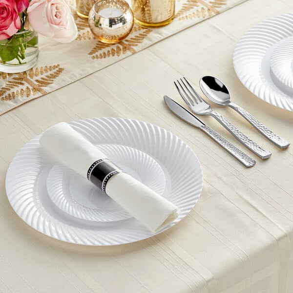 A white Wave plastic dinnerware setting with Visions silver rolled flatware on a table with flowers.