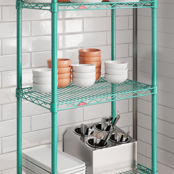 A green wire shelf unit with stacked bowls, plates, and a utensil holder.