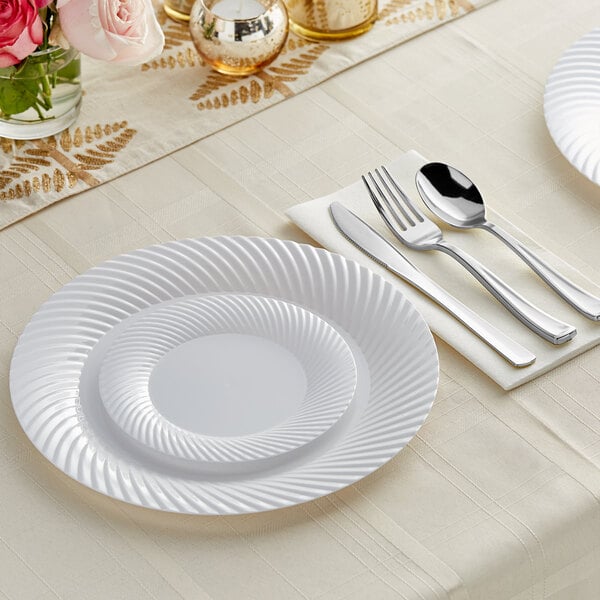 A Visions white plastic dinner plate with silver classic flatware on a white napkin.