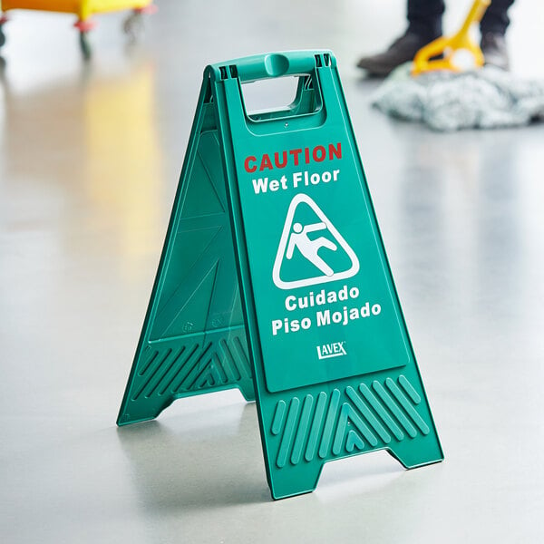 A person standing next to a green Lavex Caution Wet Floor sign.