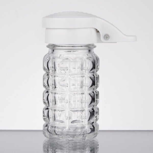A Tablecraft glass shaker with a white lid on a table.
