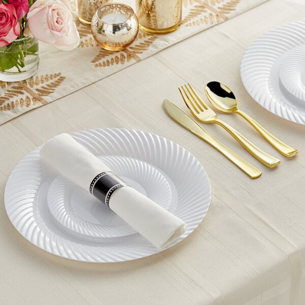 A white table setting with Visions white plates, gold and silver flatware, and a rolled napkin.