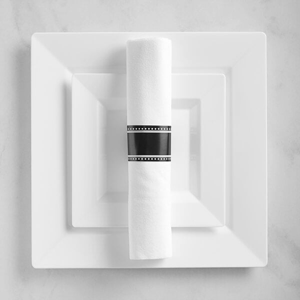 A white rectangular plate with a rolled up black napkin and silverware on it.