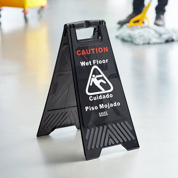 A black Lavex caution wet floor sign on a white floor.