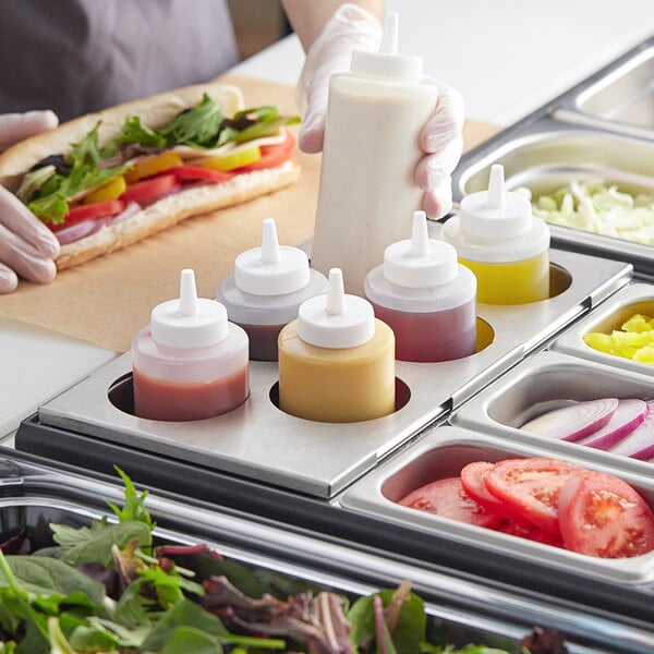 A person holding a Choice stainless steel squeeze bottle of sauce over a salad bar.