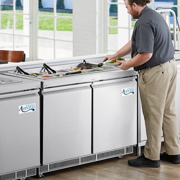 A man serving food from an Avantco stainless steel refrigerated salad bar.