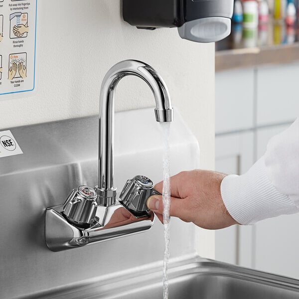 A person washing their hands in a sink using a gooseneck faucet with a white surface.