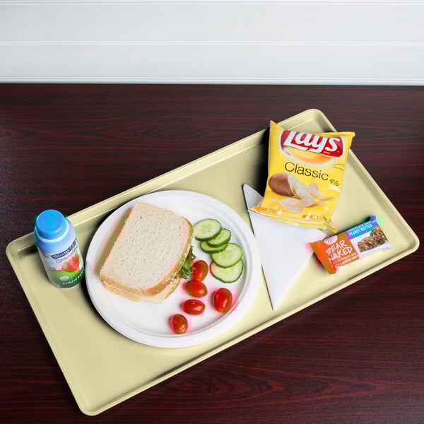 A Cambro lemon chiffon dietary tray with a sandwich, chips, and a blue drink on it.