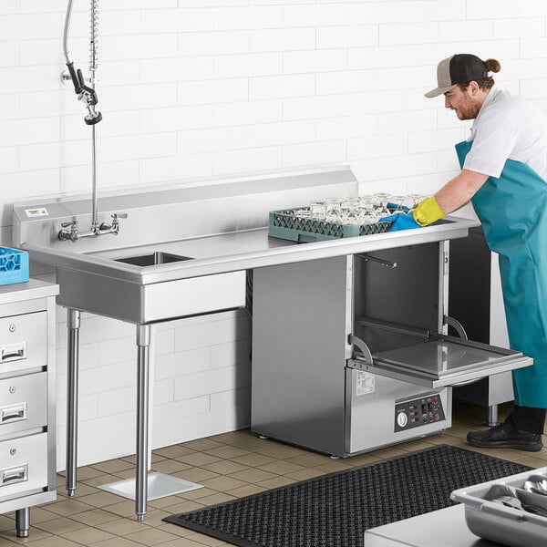 A man in a blue uniform and gloves cleaning dishes on a Regency stainless steel dishtable in a professional kitchen.