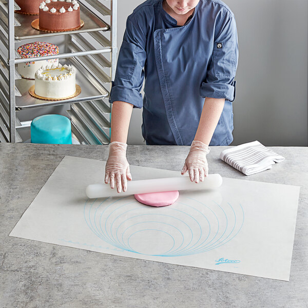 A woman using an Ateco silicone work mat with circular measurements to roll out pink dough on a white table.