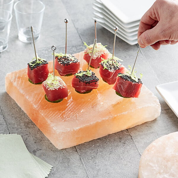 A hand holding a toothpick of food on a Himalayan salt slab.