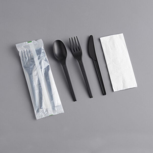 A black EcoChoice CPLA spoon with a fork, knife, and napkin.