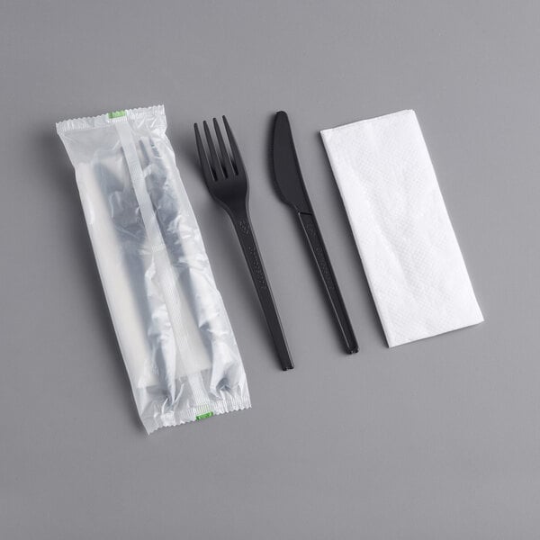 A wrapped black EcoChoice CPLA fork, knife, and napkin on a gray surface.