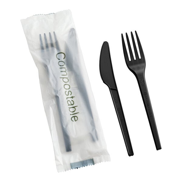 A set of black compostable heavy weight knife and fork, with one set wrapped in packaging labeled 'Compostable.'
