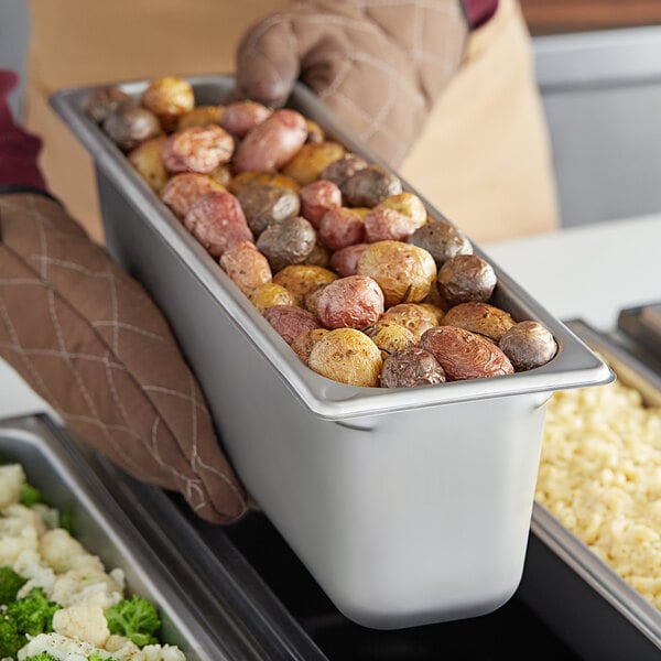 A person holding a Vigor stainless steel pan of potatoes.