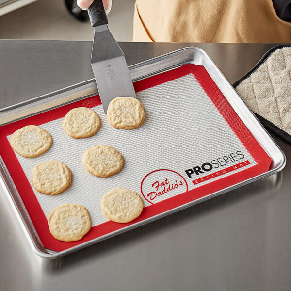 A person using a Fat Daddio's silicone baking mat to cut cookies on a tray.