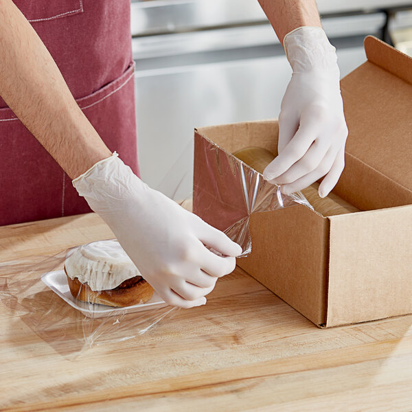 A person wearing gloves uses Western Plastics perforated plastic wrap to package pastries.