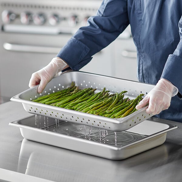 A person in a white coat holding a Vigor stainless steel steam table pan full of asparagus.