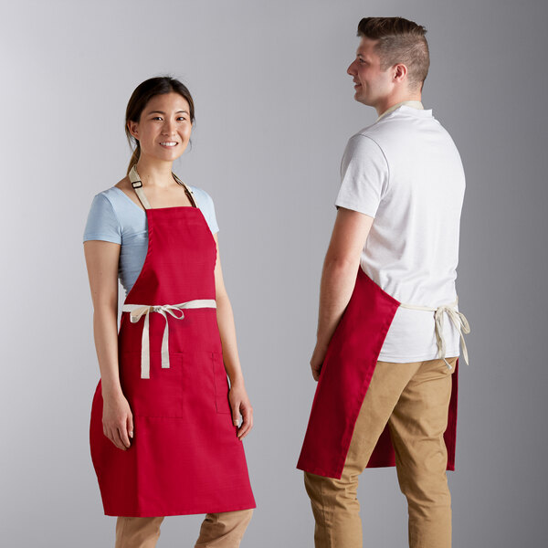 A man and woman wearing Choice red aprons standing next to each other on a counter in a professional kitchen.