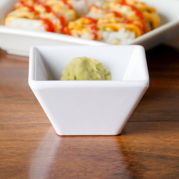 A white square bowl with green food in it.