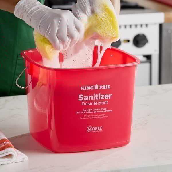 A red Noble King-Pail 8 quart sanitizing pail being used with a sponge and gloves.