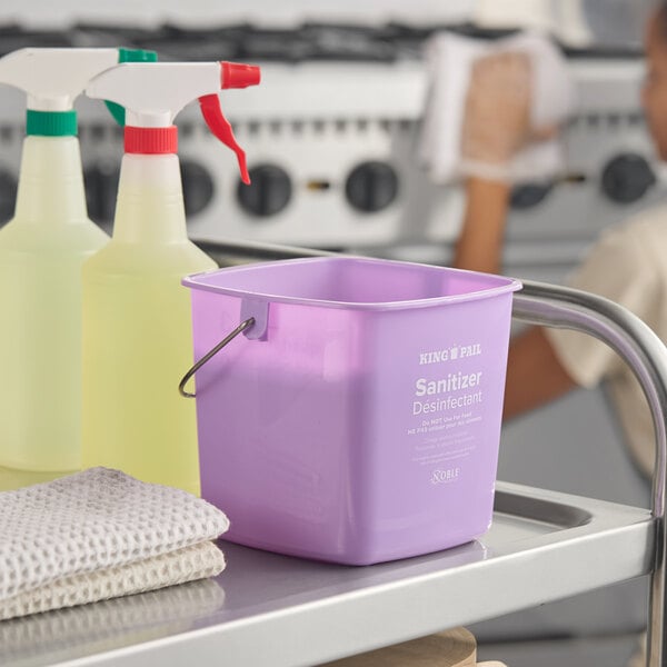 A purple Noble King-Pail 3 quart allergen-free sanitizing pail on a metal cart next to cleaning supplies.