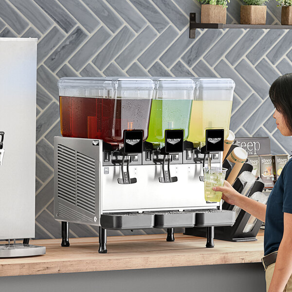 A woman standing at a counter with a Vollrath refrigerated beverage dispenser.