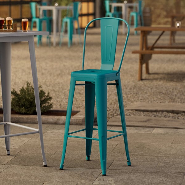 A close-up of a Lancaster Table & Seating teal barstool on an outdoor patio.