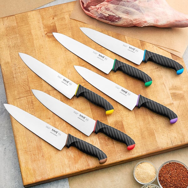 A Schraf chef knife with a green handle on a cutting board with four other knives.