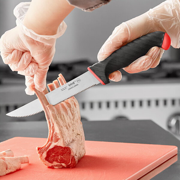 A hand holding a Schraf serrated utility knife to cut meat on a cutting board.