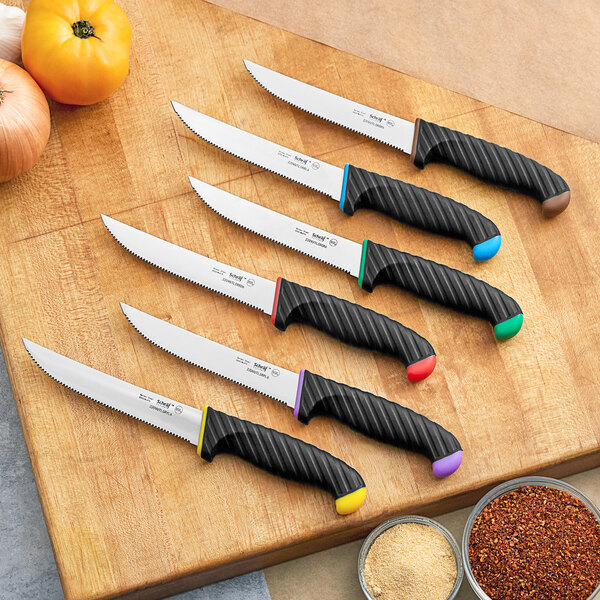 A Schraf serrated utility knife with a green handle on a table with a group of knives.