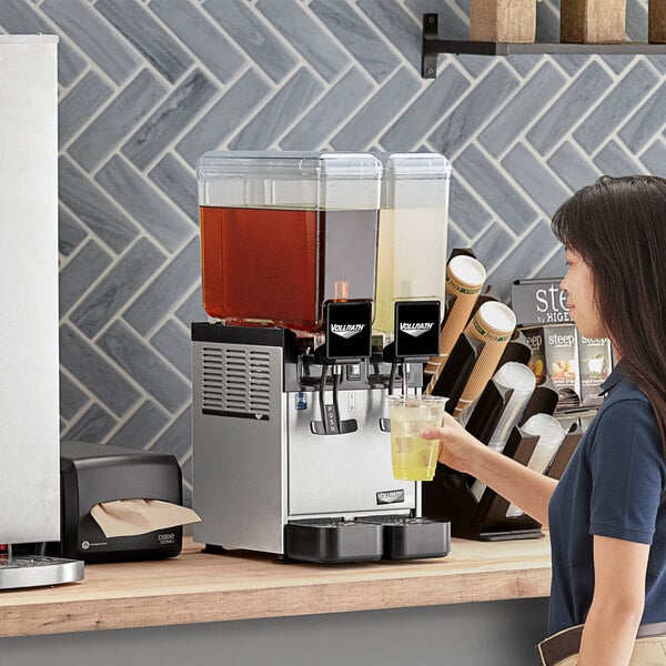 A woman pouring liquid into a Vollrath refrigerated beverage dispenser.