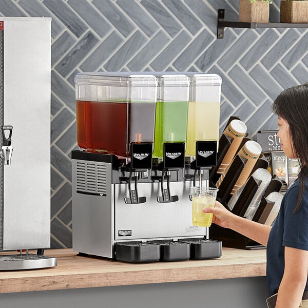 A woman pouring yellow liquid into a Vollrath refrigerated beverage dispenser.