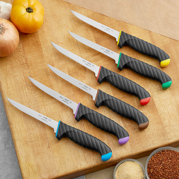A group of Schraf knives with red, yellow, and black handles on a cutting board.