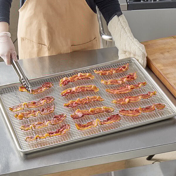 A woman using tongs to place bacon on a Choice chrome footed cooling rack.