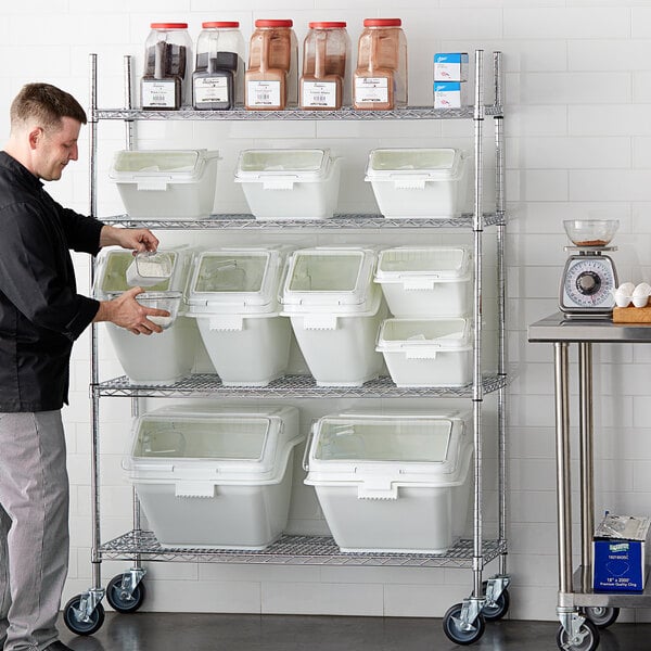 A man standing next to a shelf with Baker's Lane white plastic ingredient bins with clear flip lids.