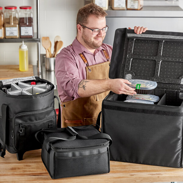 A man in an apron opening a black ServIt delivery bag.