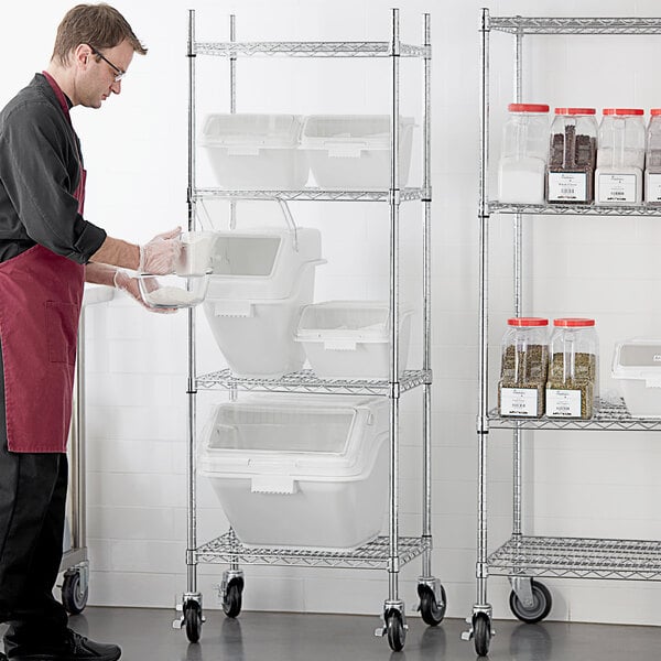 A man wearing a red apron and gloves standing next to a white shelf holding white Baker's Lane ingredient bins.