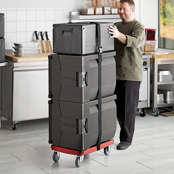 A man using a red dolly to move a stack of black CaterGator pan carriers.