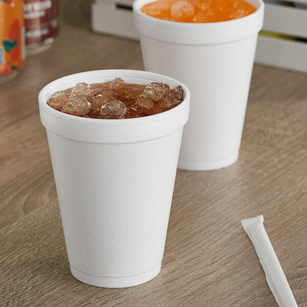 Two Dart white foam cups filled with ice and orange juice on a wood surface.