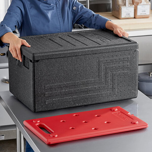 A woman holding a black plastic CaterGator food pan carrier on a counter in a professional kitchen.