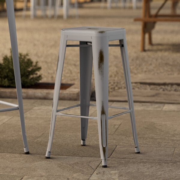 Lancaster Table & Seating Distressed Nickel Gray Outdoor Backless Barstools sitting on a stone surface.