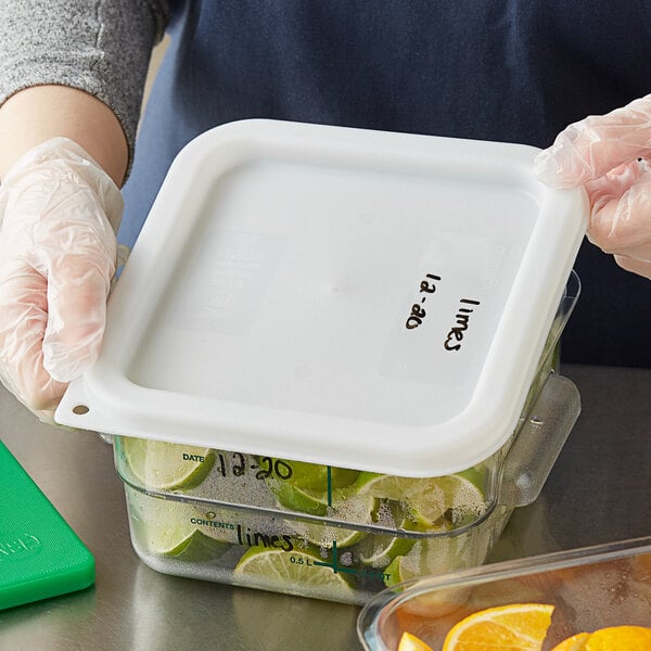 A person holding a white Vigor square polypropylene container filled with limes.