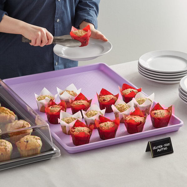A woman placing a purple Choice Bakery tray with muffins on a table.