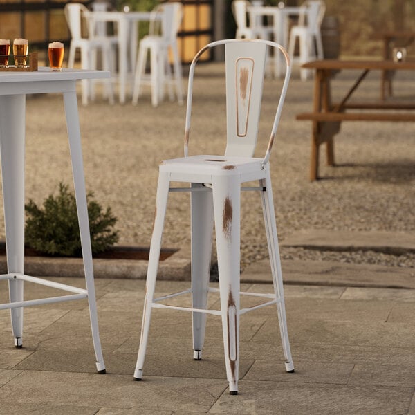 A white Lancaster Table & Seating outdoor cafe barstool on a patio with drinks on a table.