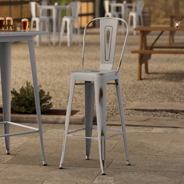 A Lancaster Table & Seating distressed nickel outdoor barstool on an outdoor patio table.