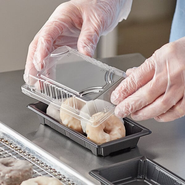A small rectangular food container with a clear plastic lid being closed over pastries by a person wearing gloves.